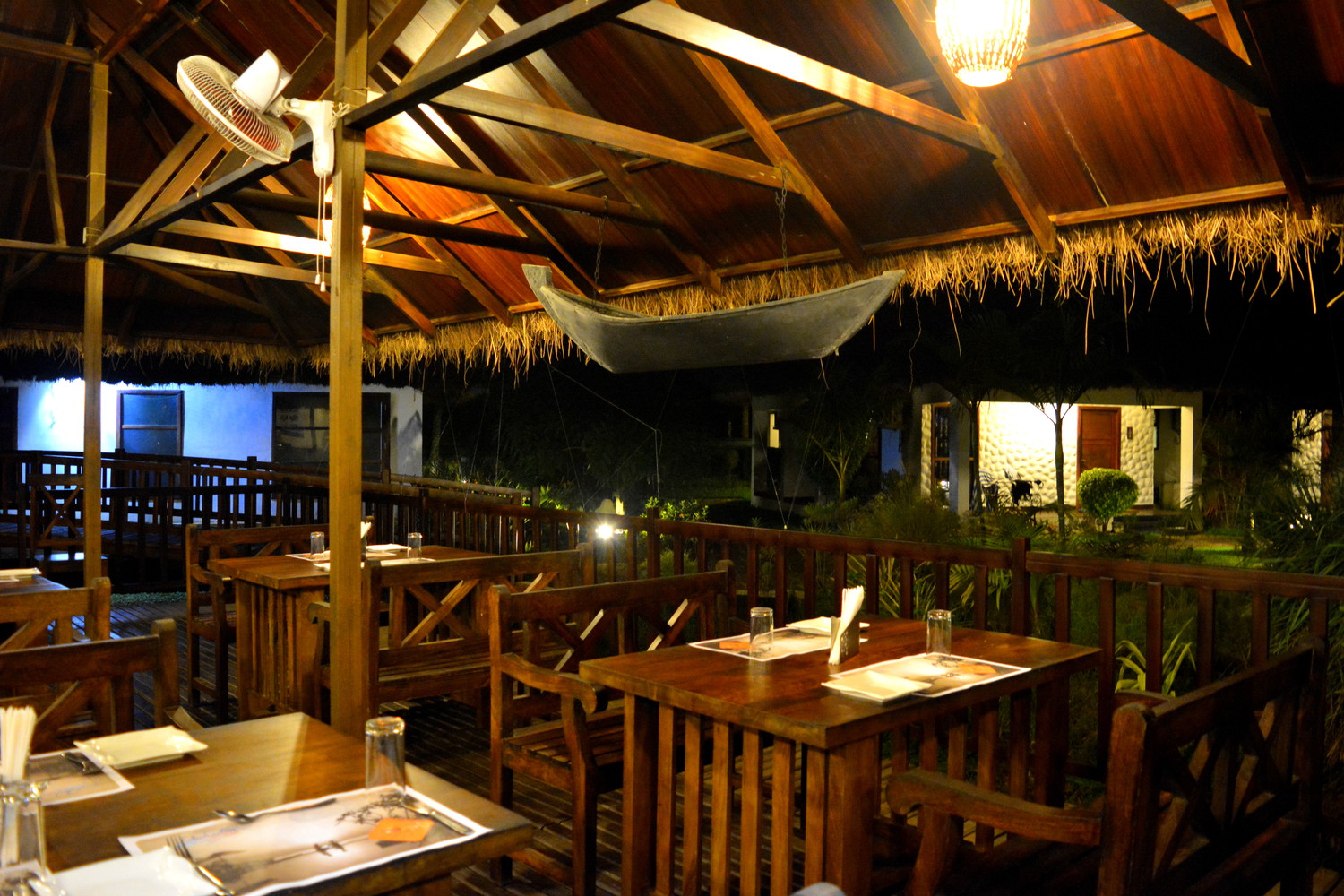 Interior of a floating restaurant with a small boat hanging at the top from the ceiling and wooden chairs and tables dimly lit in the evening