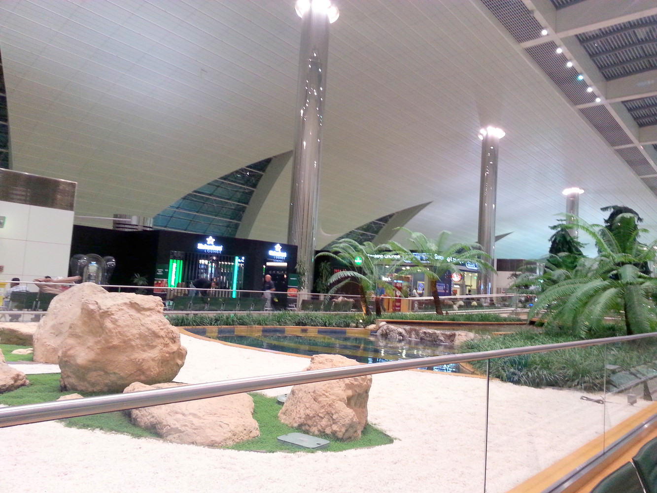 An indoor garden consisting of rocks, tiny pools, and palm trees at the terminal of an airport