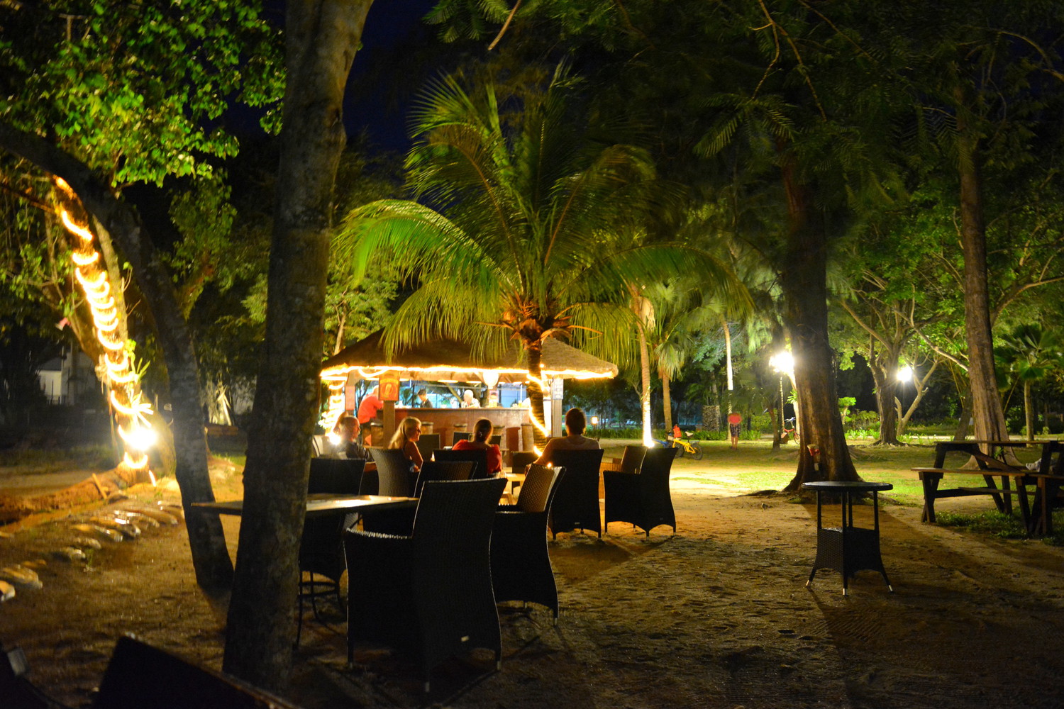 A beachside open air restaurant lit with orange lamps in the evening