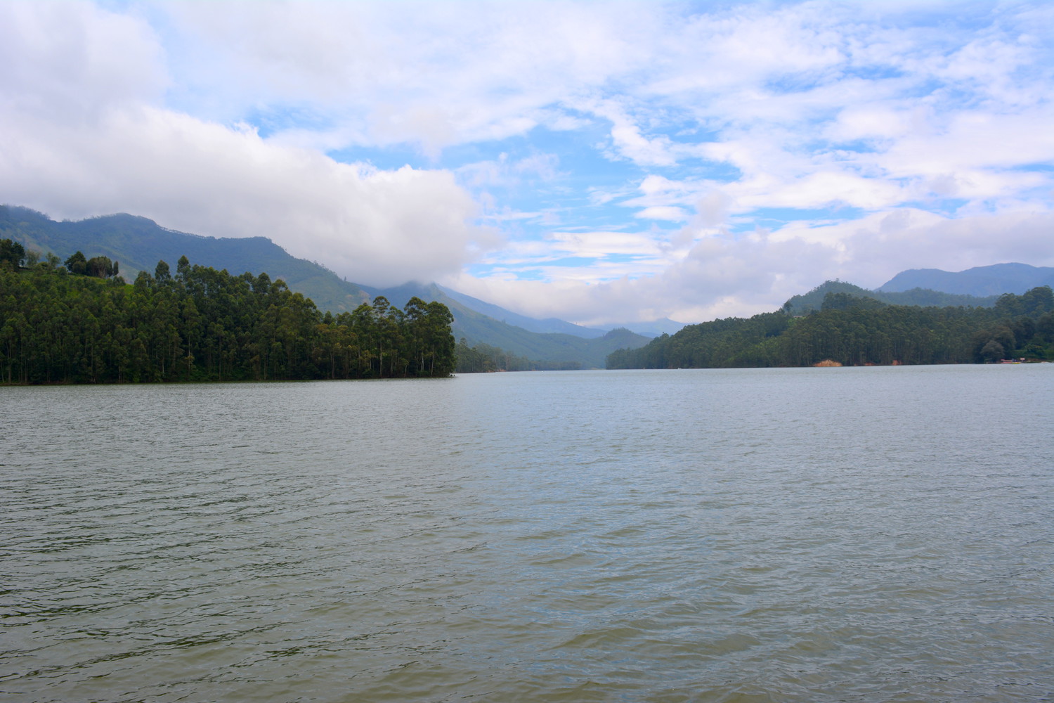 A large reservoir full of water surrounded by trees, hills, and sky in the background