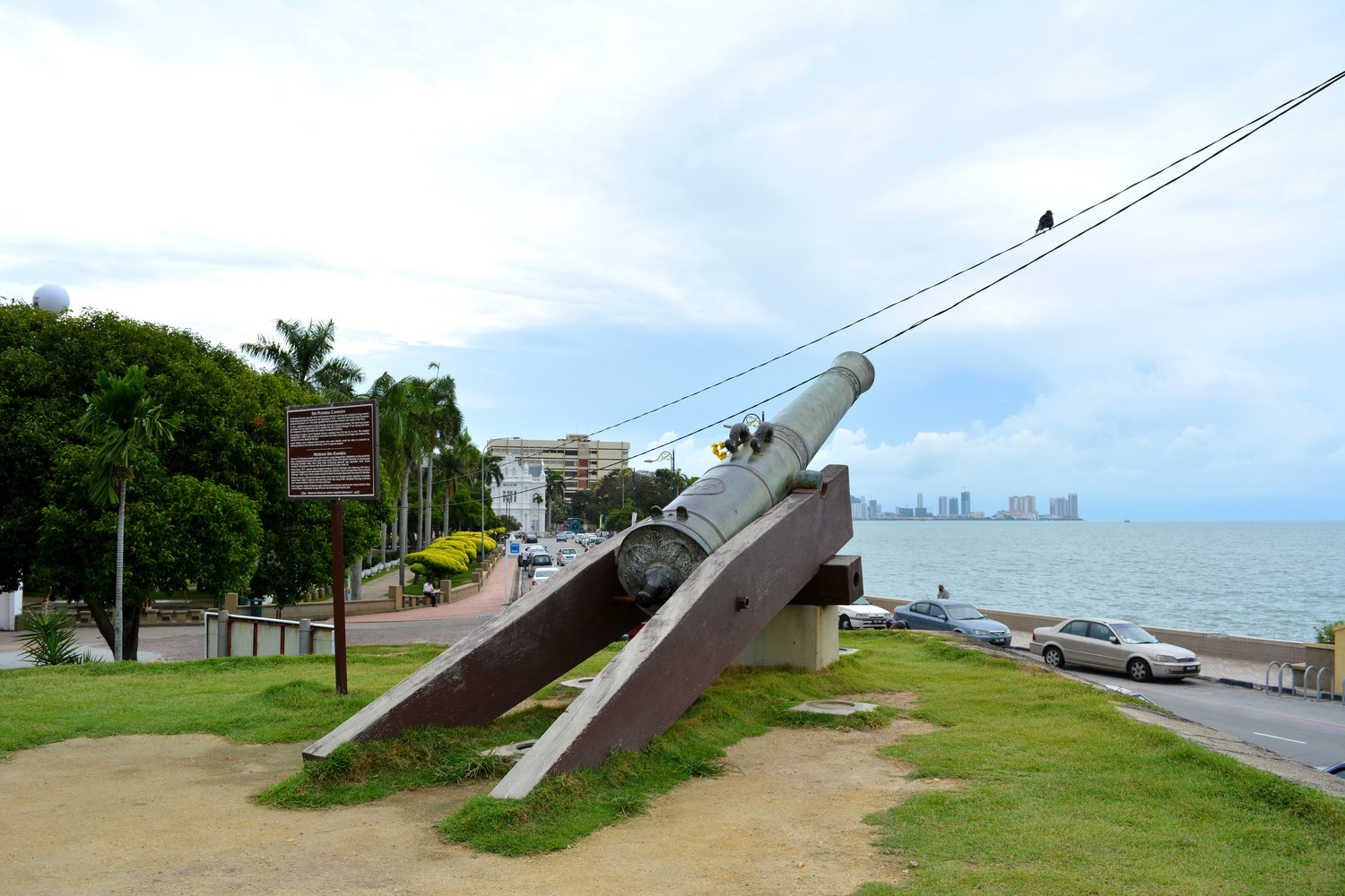 A cannon at a corner of a fort overlooking a street in front of it and the surrounding sea