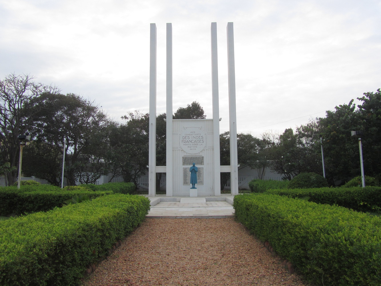 A war memorial with four white pillars, a white board with bronze plaques, and a statue