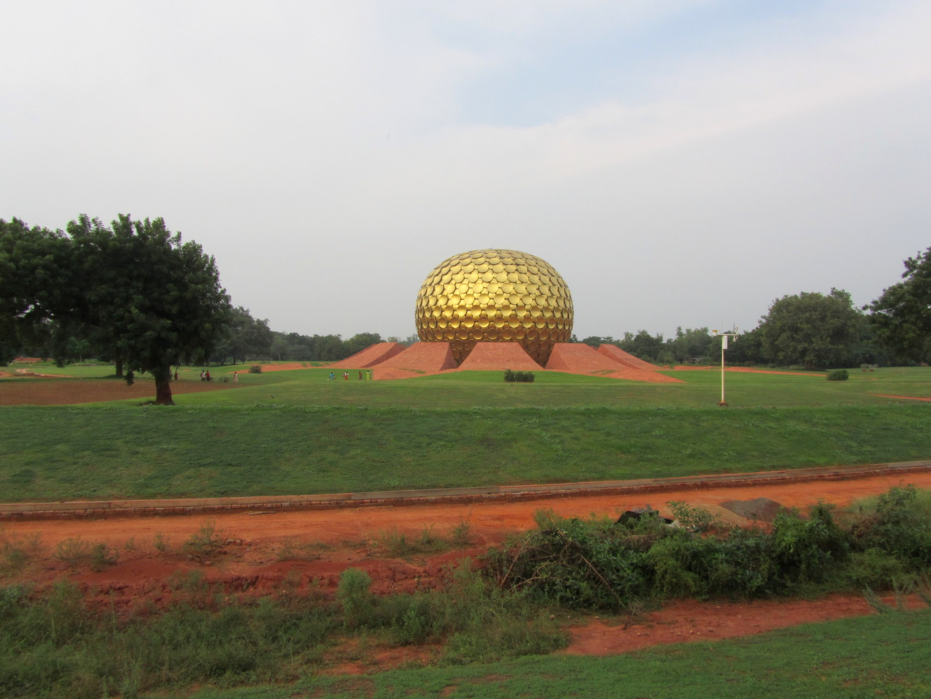 A huge golden metallic sphere supported by large orange petals at the centre of a large green lawn