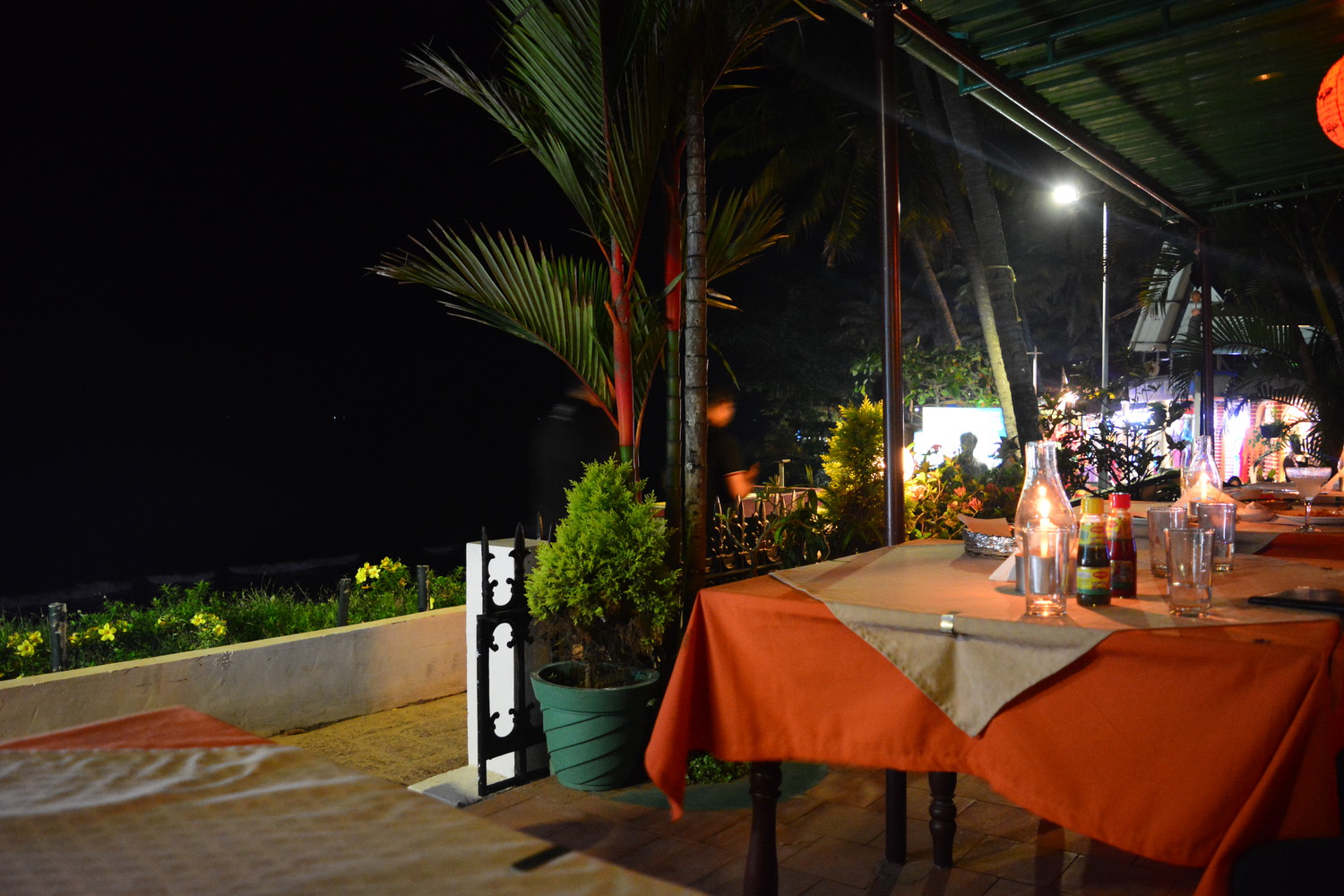 A restaurant with candlelit tables beside a promenade in the evening