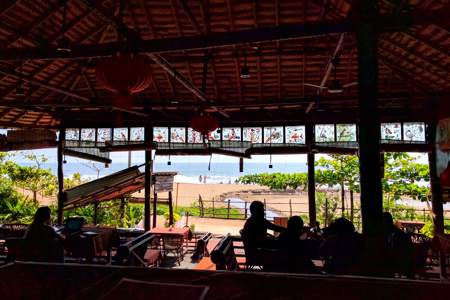 A restaurant with guests and thatched ceiling overlooking a sea beach